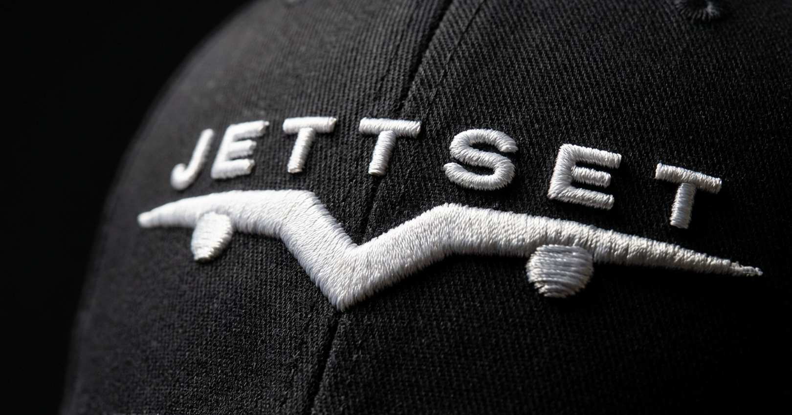 Macro shot of raised white embroidery, the Jettset wordmark and logo on a black cap, Jettset Global Editions capsule lifestyle collection